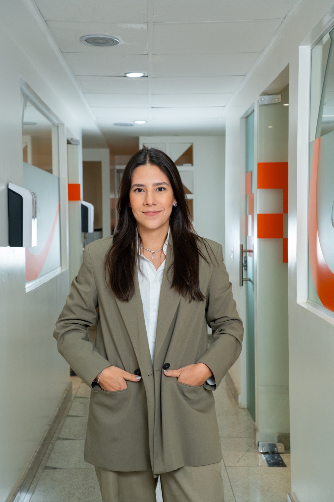 Dra. Viviane Rossi — Ortodontista em Brasília, blazer oliva, sorrindo no corredor da clínica